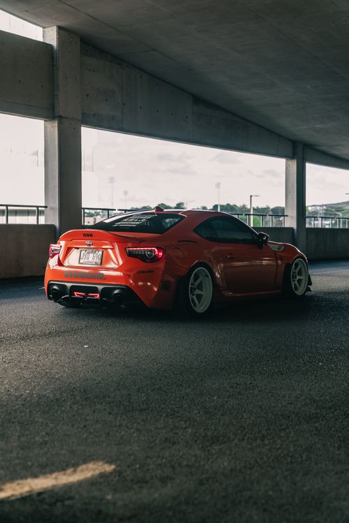 Free A dynamic red sports car with sleek lines parked in an urban garage, showcasing modern automotive design. Stock Photo