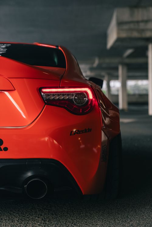 Free Close-up of a sleek orange sports car's rear under a dimly lit parking structure. Stock Photo