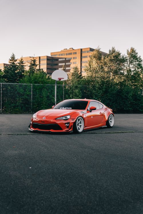 Free Custom red sports car parked on a basketball court with urban buildings in the background. Stock Photo