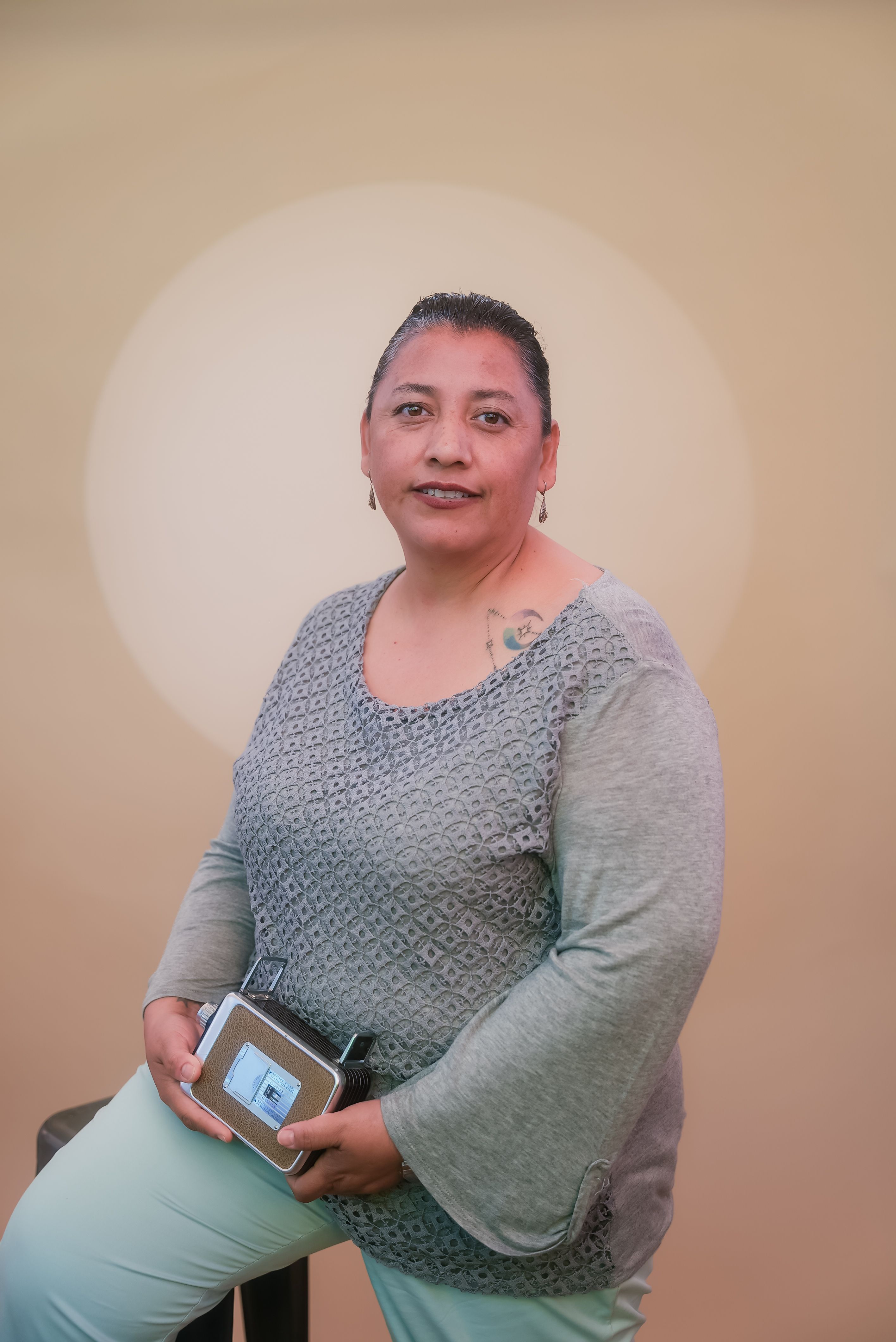 Confident adult woman seated indoors holding a tablet with a neutral background.