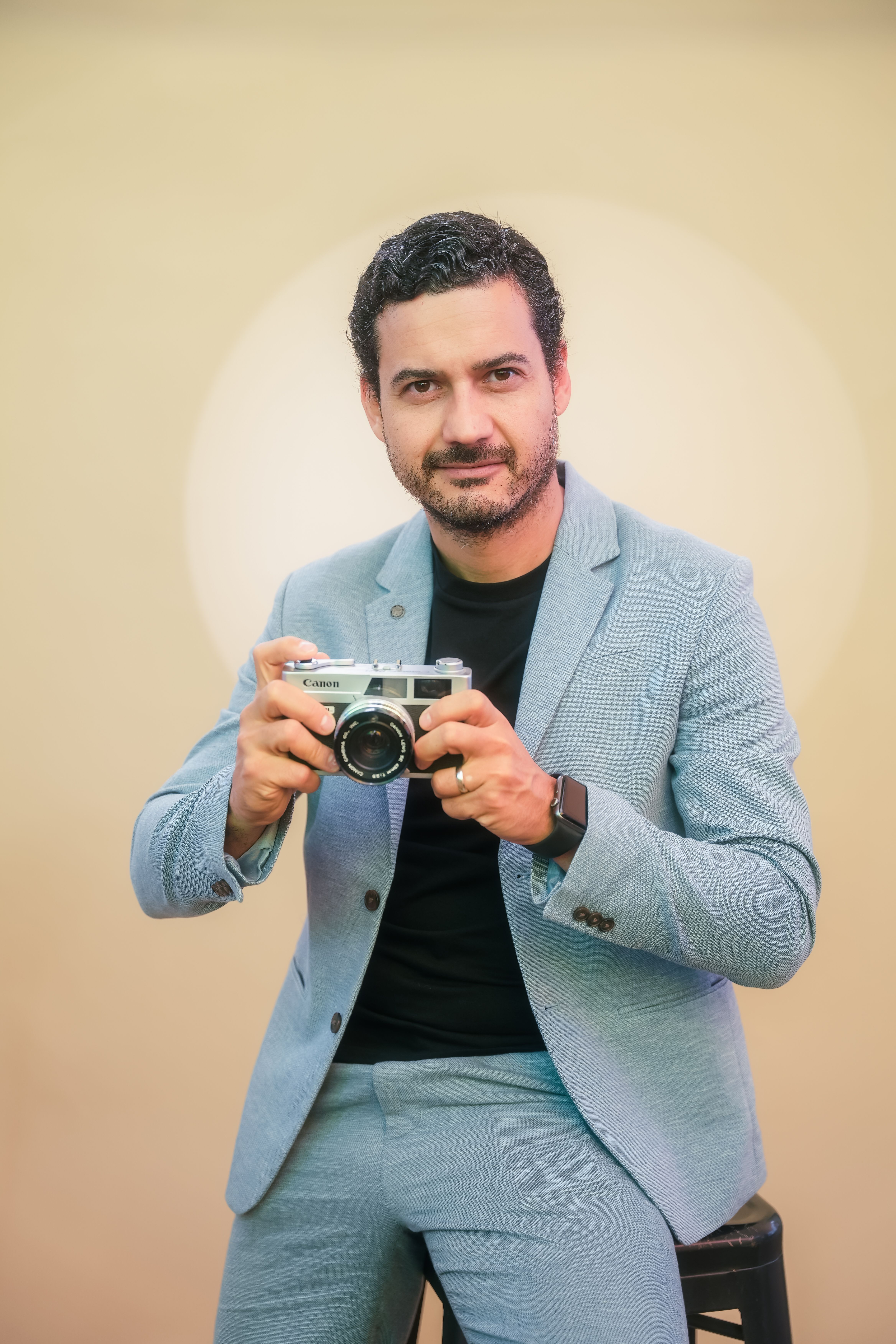 Portrait of a man in blue suit holding a vintage camera, exuding style and charm.