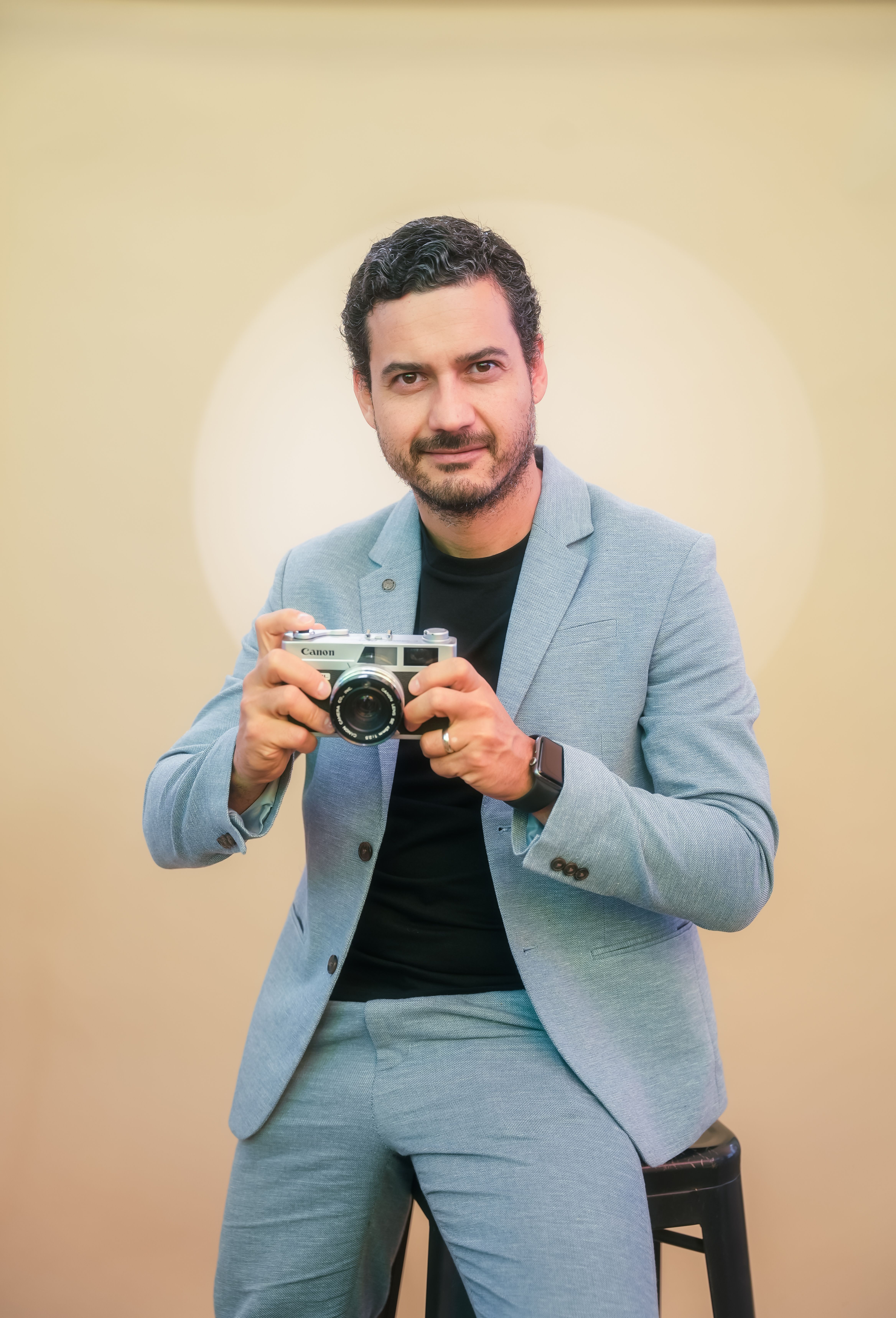 Professional photographer posing with a vintage camera in a stylish blue suit.