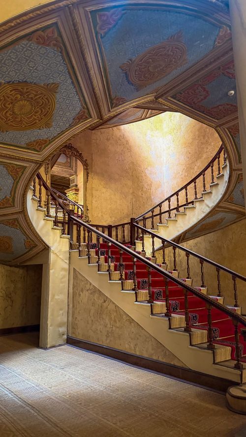 Free Captivating view of a grand spiral staircase with luxurious red carpet in a historic interior. Stock Photo