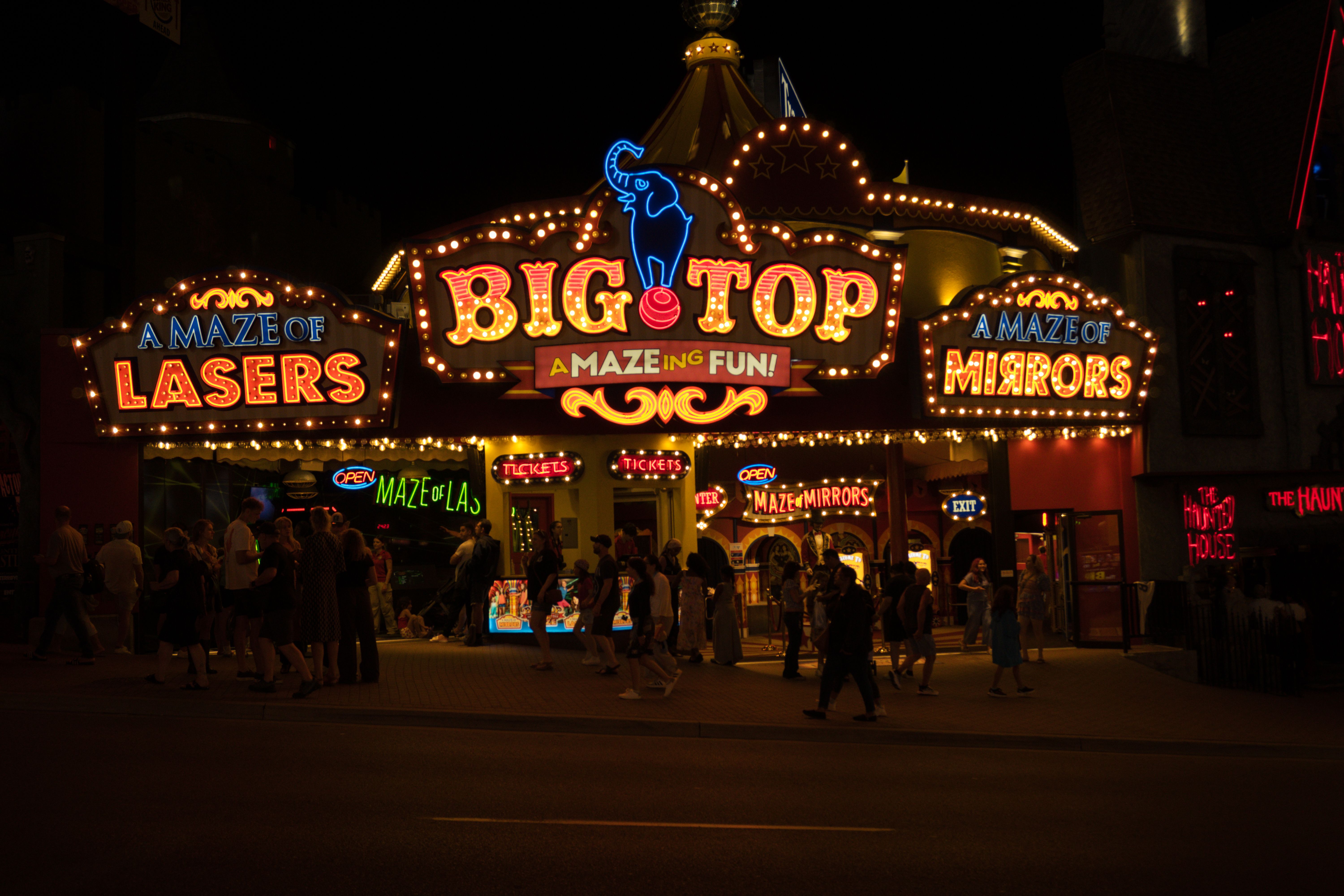 Vibrant neon-lit entrance to amusement park attractions including mirror maze and laser maze.