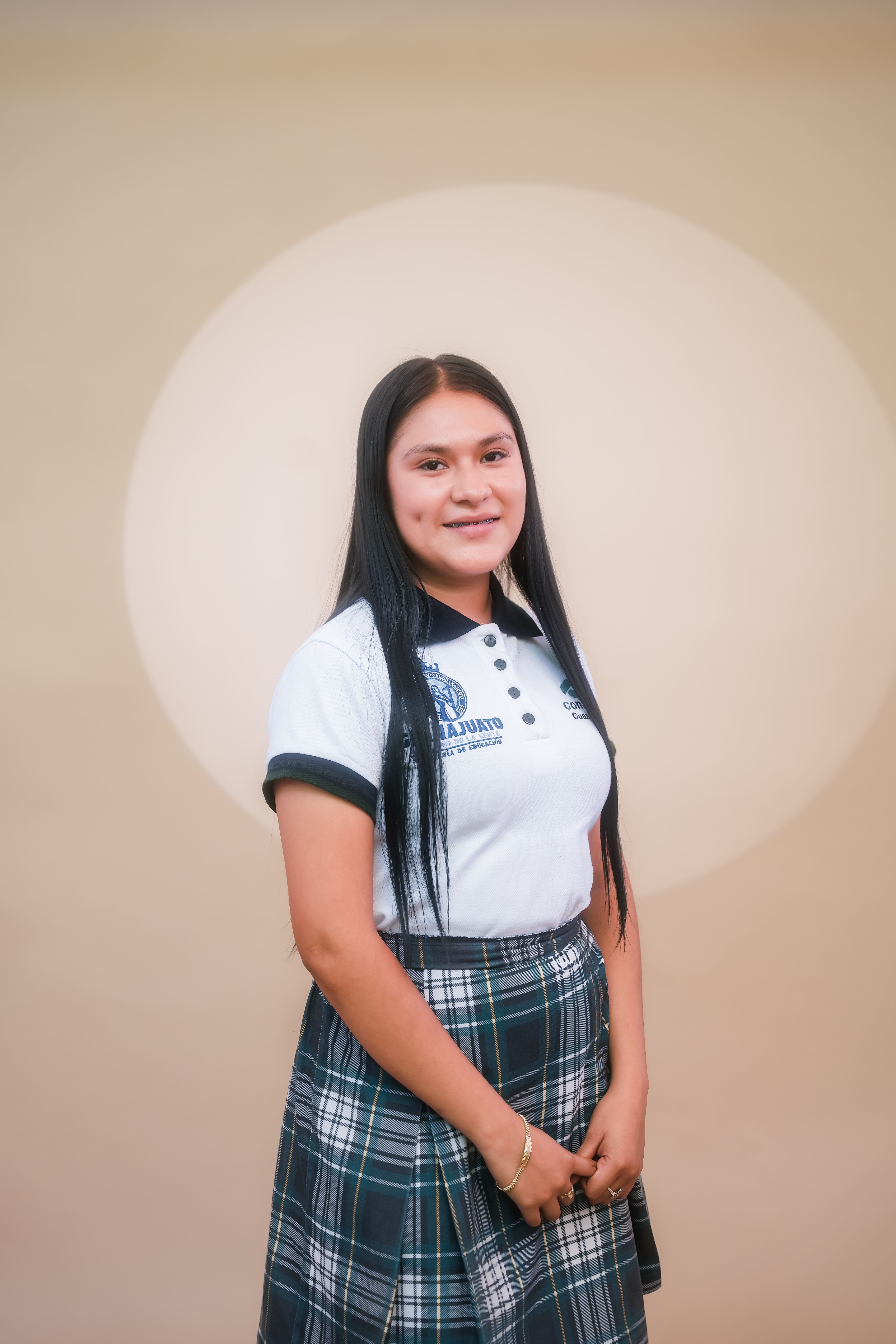Portrait of a young woman in a school uniform, smiling against a neutral backdrop, Irapuato, Mexico.