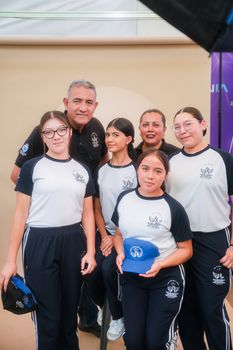 A diverse group of students and an adult smiling indoors, wearing athletic uniforms.