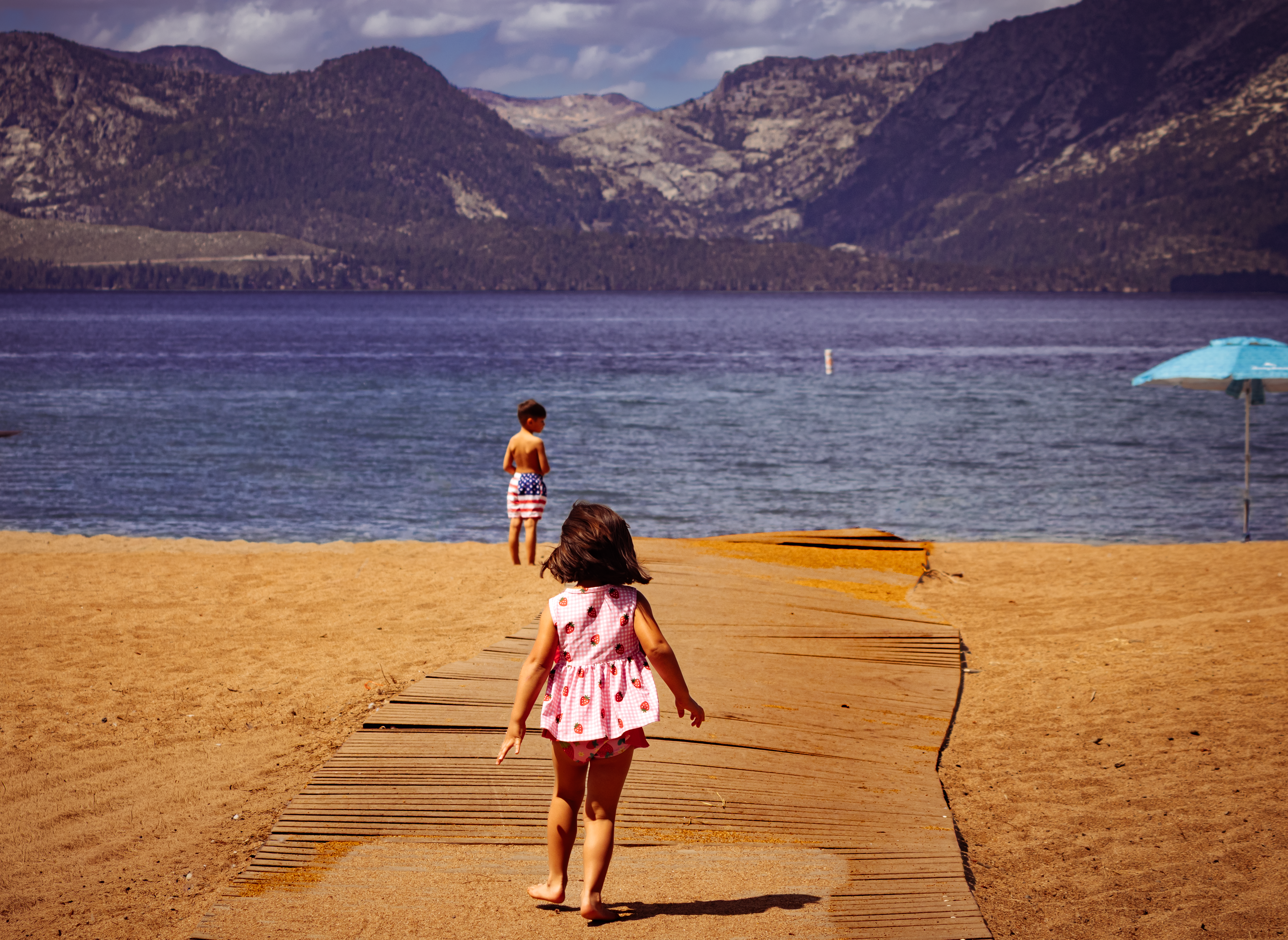 Two children playing on a sandy beach with mountains behind them.