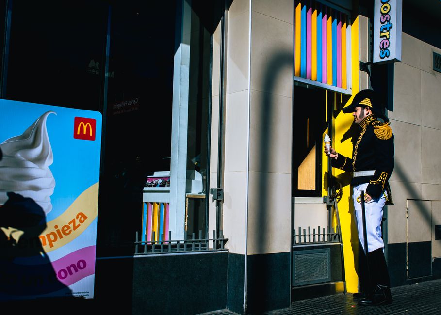 Un hombre ataviado con un traje de época disfruta de un helado frente a una colorida tienda.