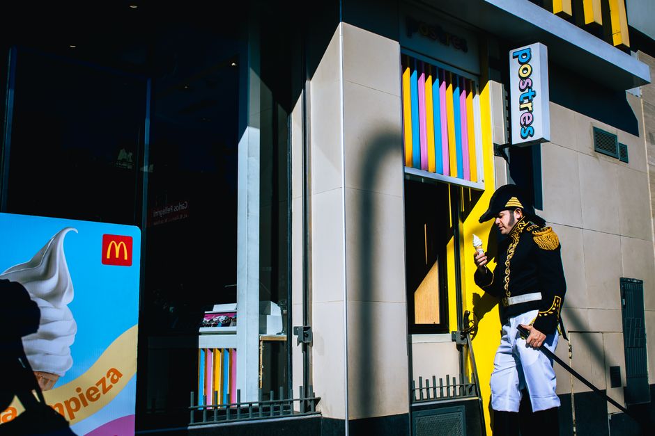 Un hombre con uniforme de época disfruta de un helado frente a un edificio colorido en un día soleado.