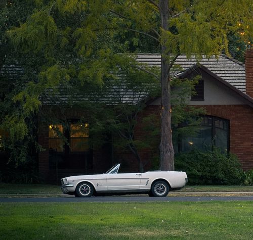 Free White convertible car parked outside a suburban house surrounded by trees, evoking a vintage and serene mood. Stock Photo
