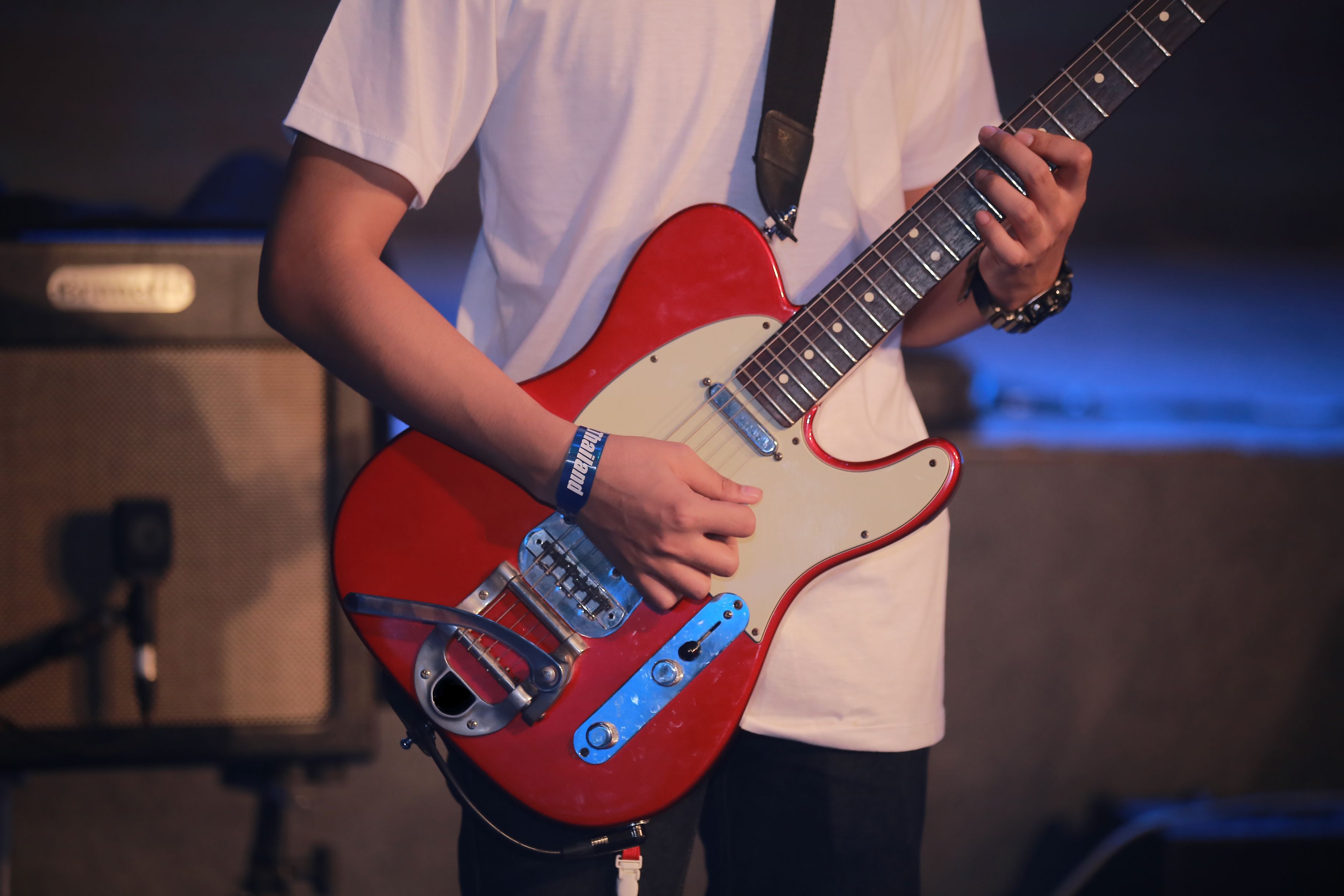 Close-up of a guitarist playing a red electric guitar during a live performance.