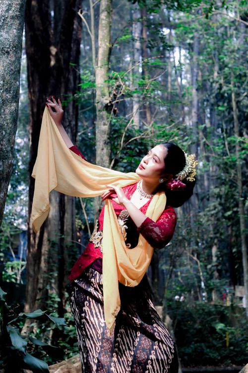 Free Portrait of a woman in traditional Indonesian attire dancing gracefully in a forest. Stock Photo