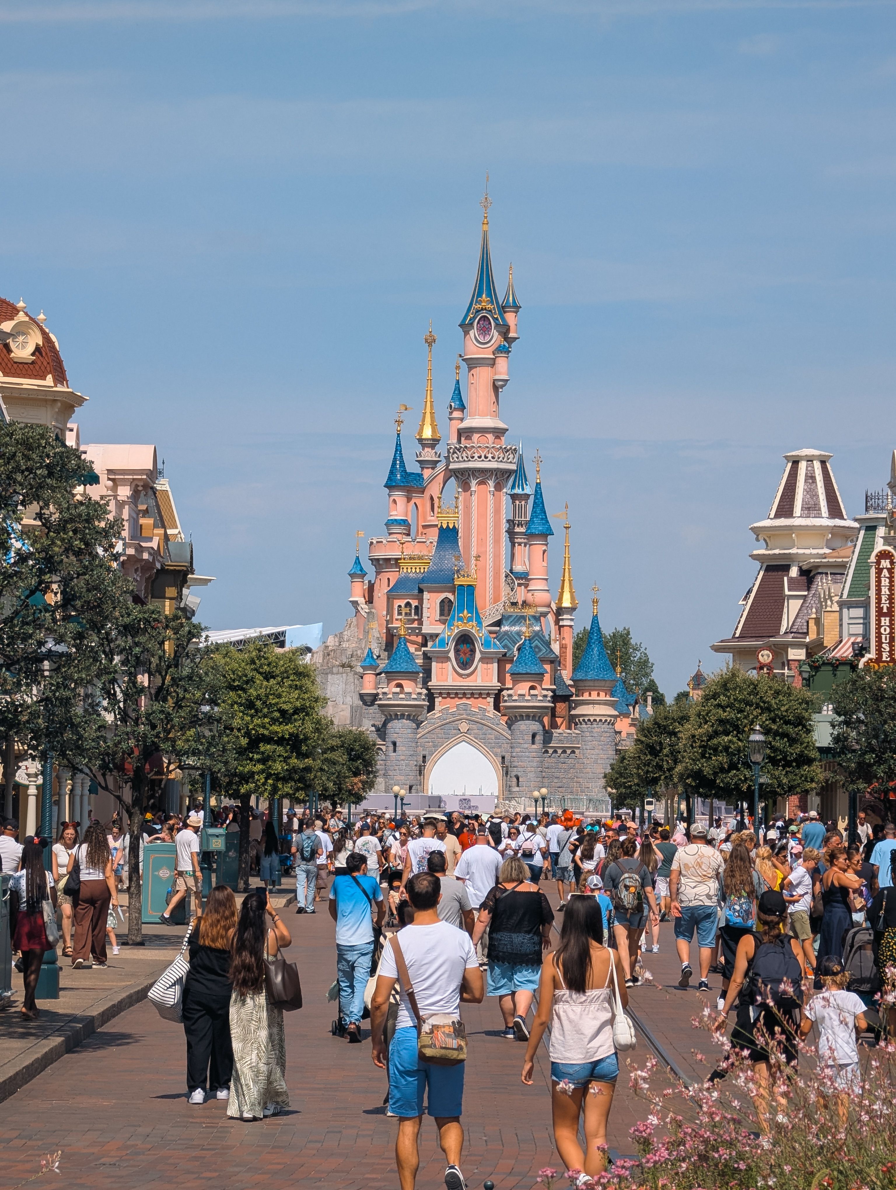Visitors enjoy a sunny day at Disneyland Paris with the Sleeping Beauty Castle in the background.