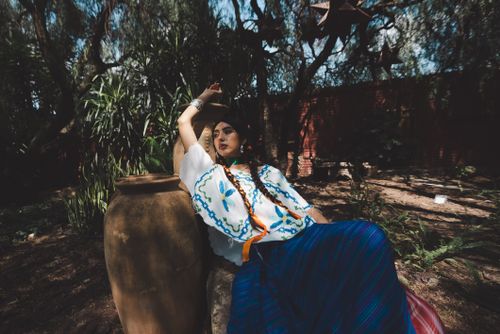 Free A woman in traditional clothing relaxes outdoors against a clay jar amid lush greenery. Stock Photo