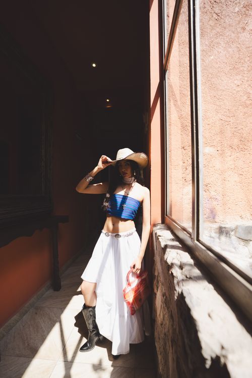 Free Woman in blue top and white skirt poses in sunlight corridor wearing a hat. Stock Photo