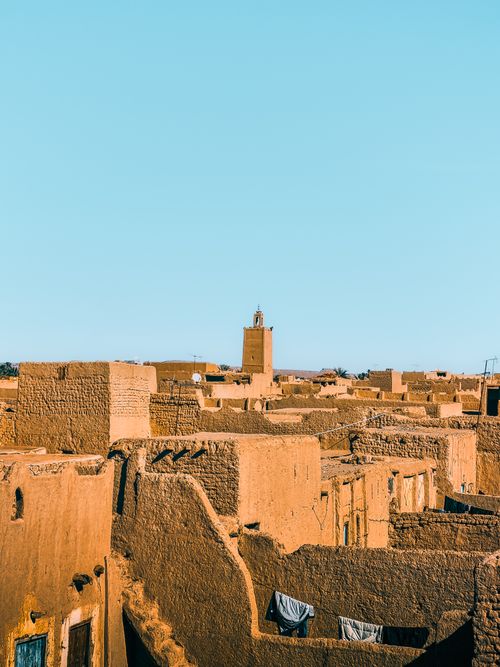 Free Scenic view of a traditional Moroccan village with adobe houses and a distant minaret under clear blue sky. Stock Photo