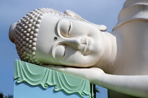 Traditional large sculpture of sleeping Buddha located against cloudless blue sky outside temple