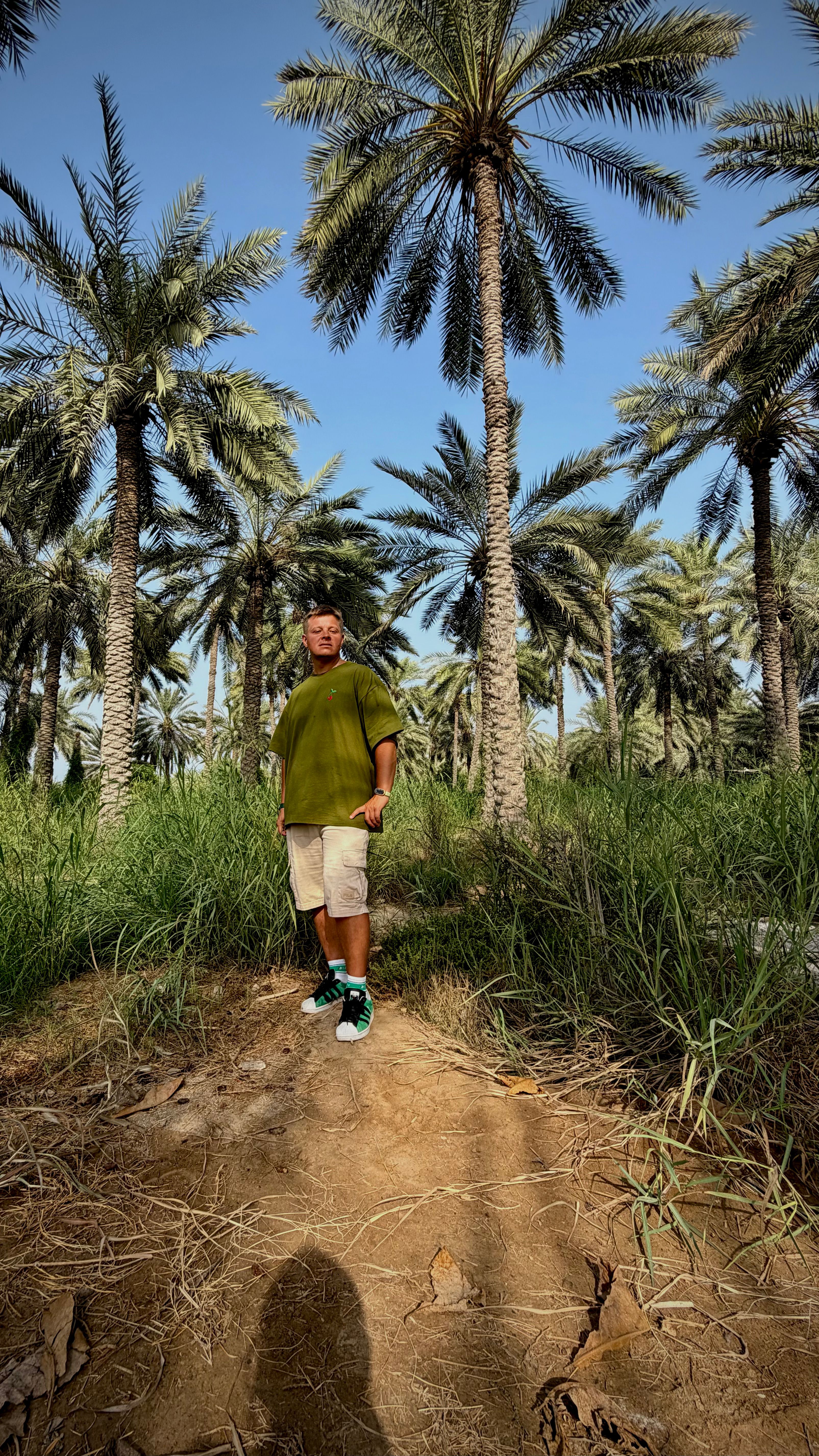 A man standing in a lush palm grove under a clear sky in Fujairah, UAE.