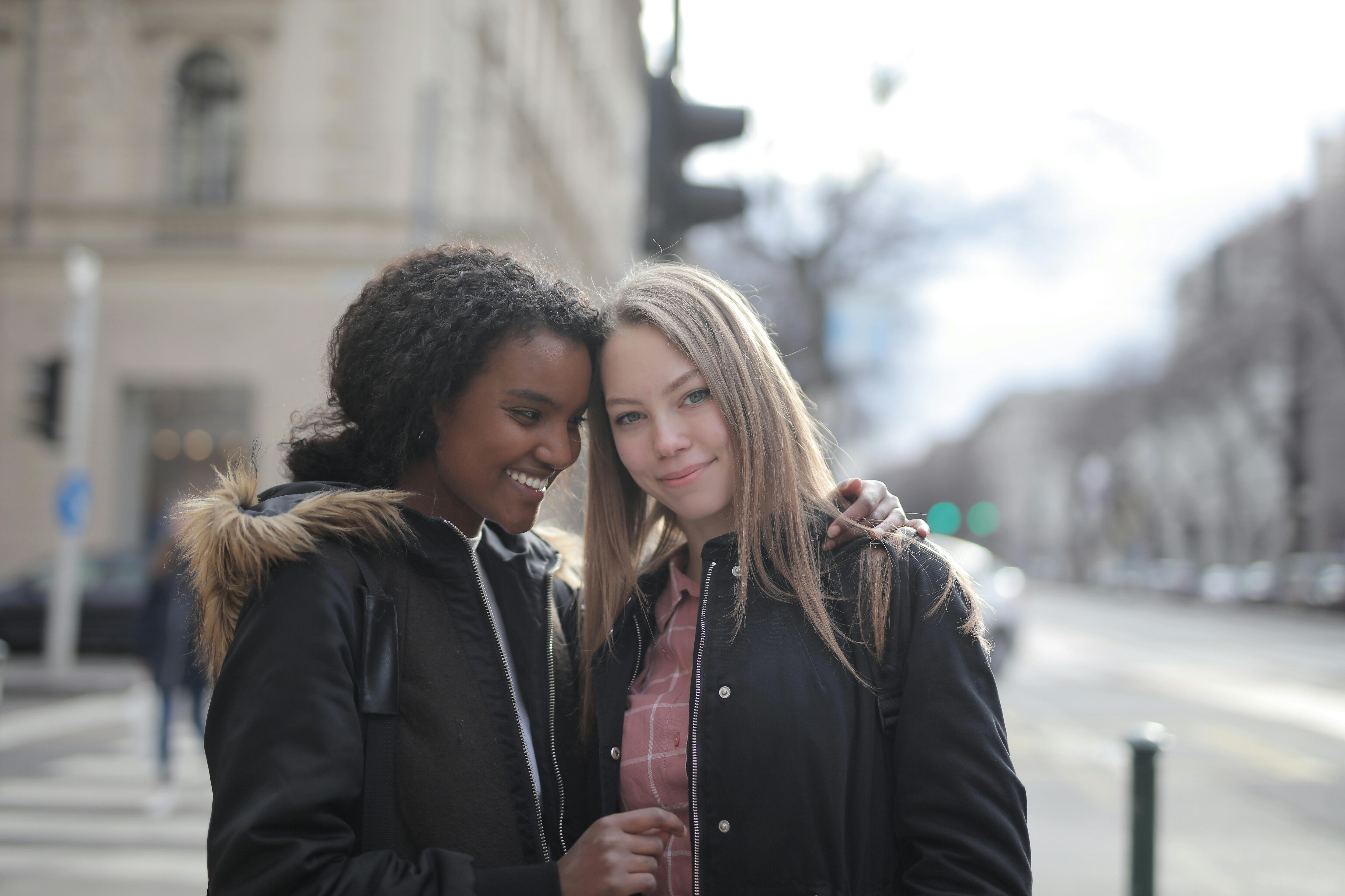 cheerful young multiracial girlfriends standing together on sidewalk on street