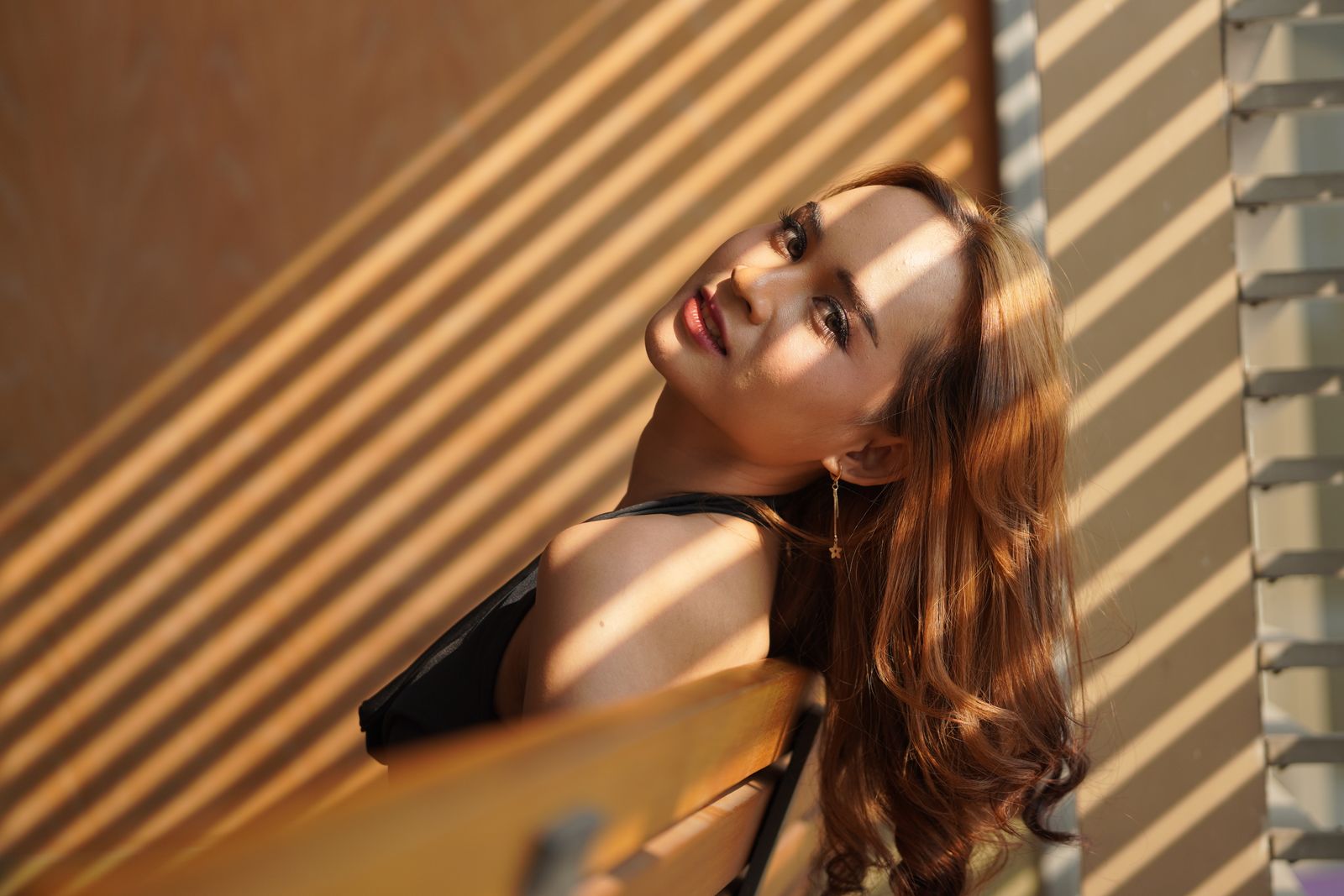 A woman posing with artistic shadows from blinds creating a serene and playful mood.