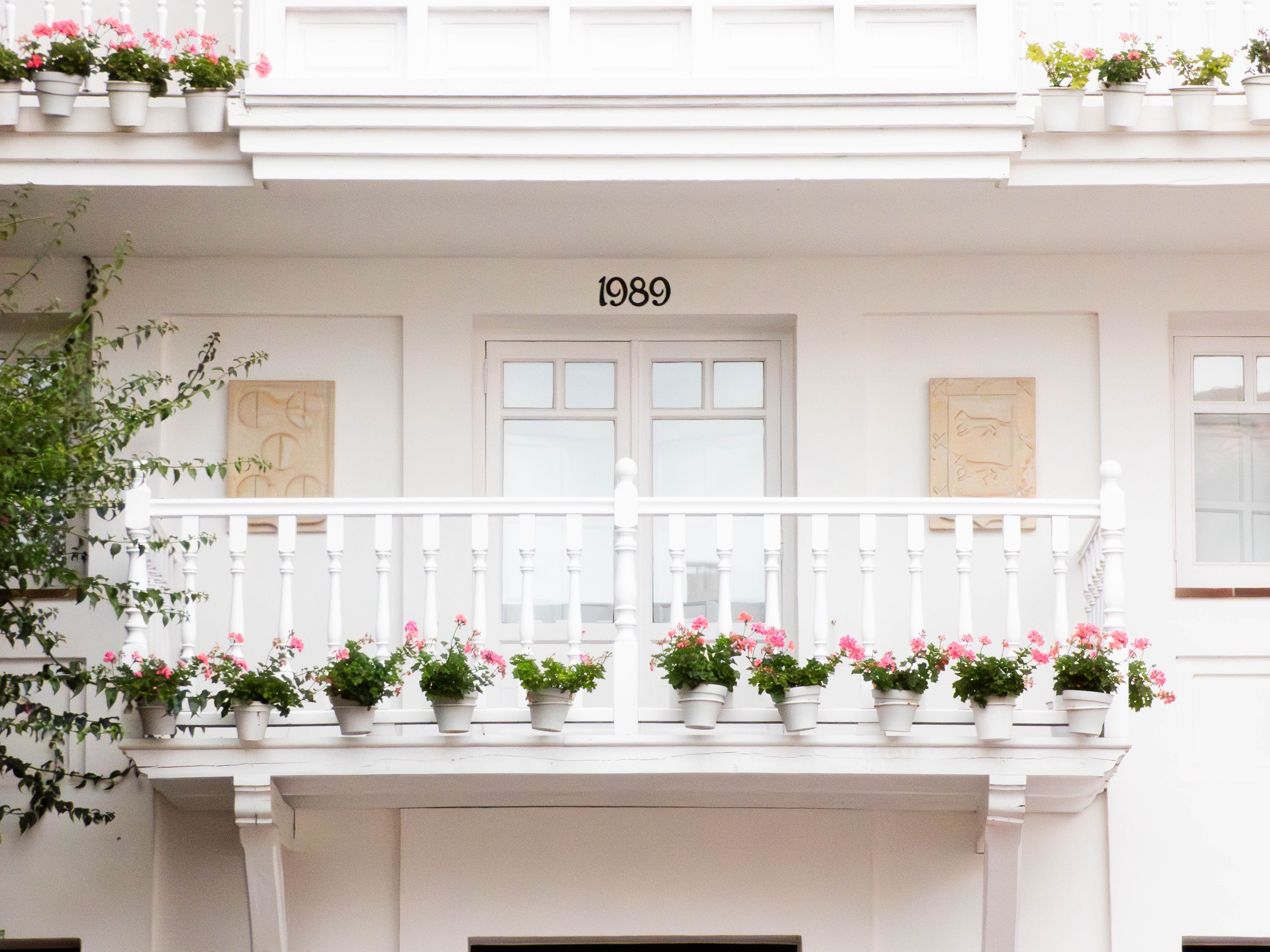 White balcony in Comillas, Spain adorned with pink flowers. Elegant minimalist exterior from 1989.
