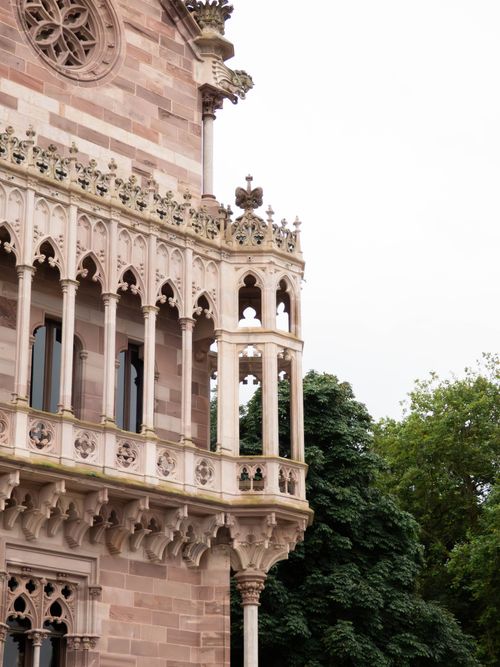 Free Detailed view of Gothic Revival architecture in Comillas, showcasing ornate stonework and lush greenery. Stock Photo