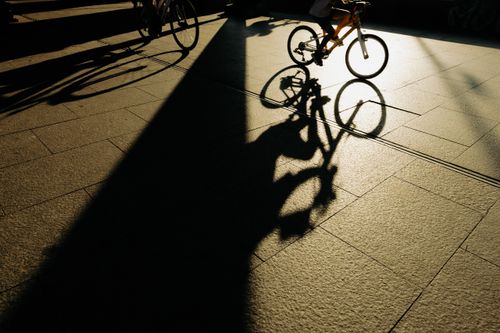 Free A cyclist's shadow on sunny pavement, capturing dynamic motion and light contrasts. Stock Photo