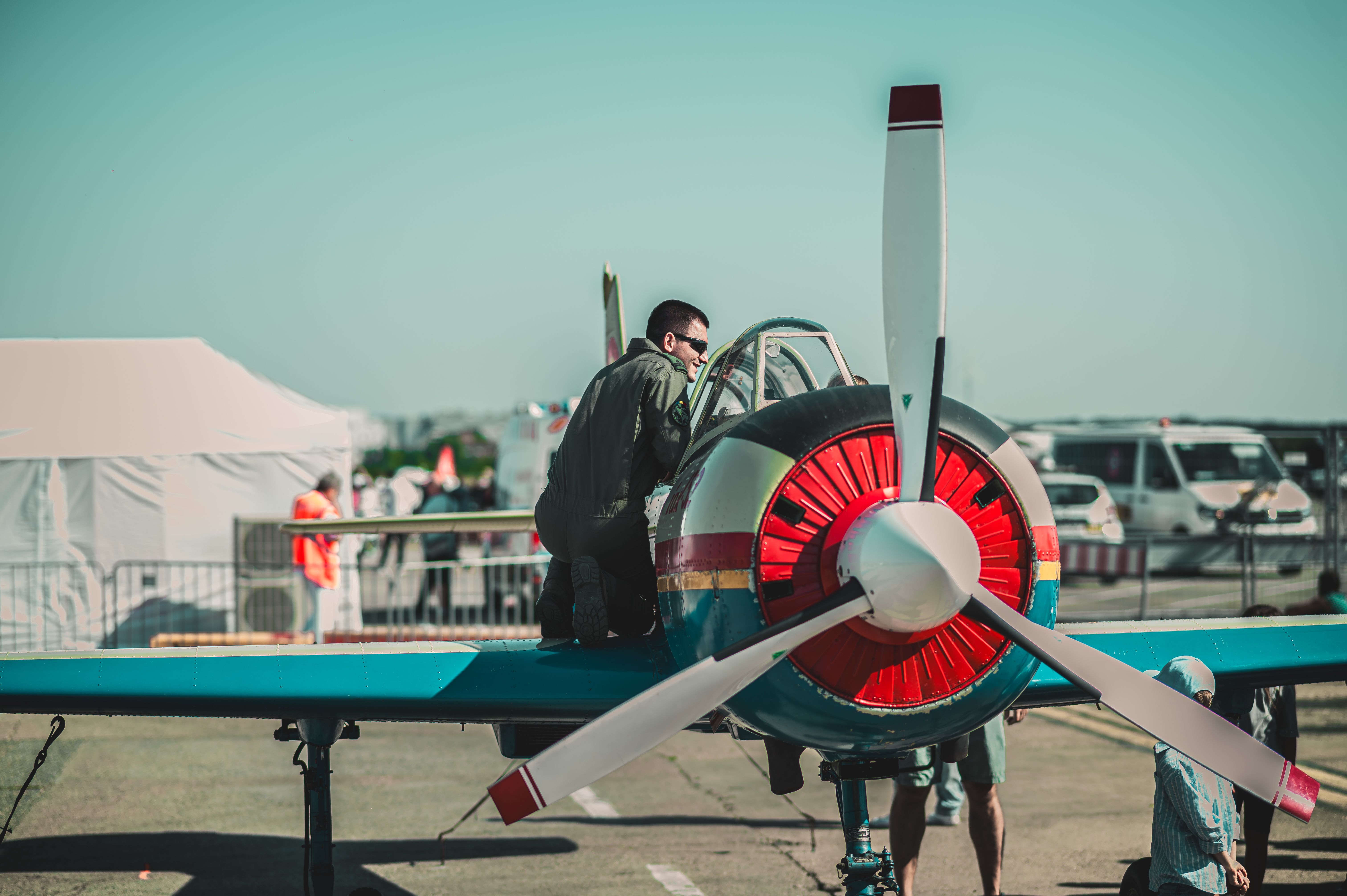 A pilot wearing sunglasses prepares a propeller aircraft for flight at an outdoor airshow.
