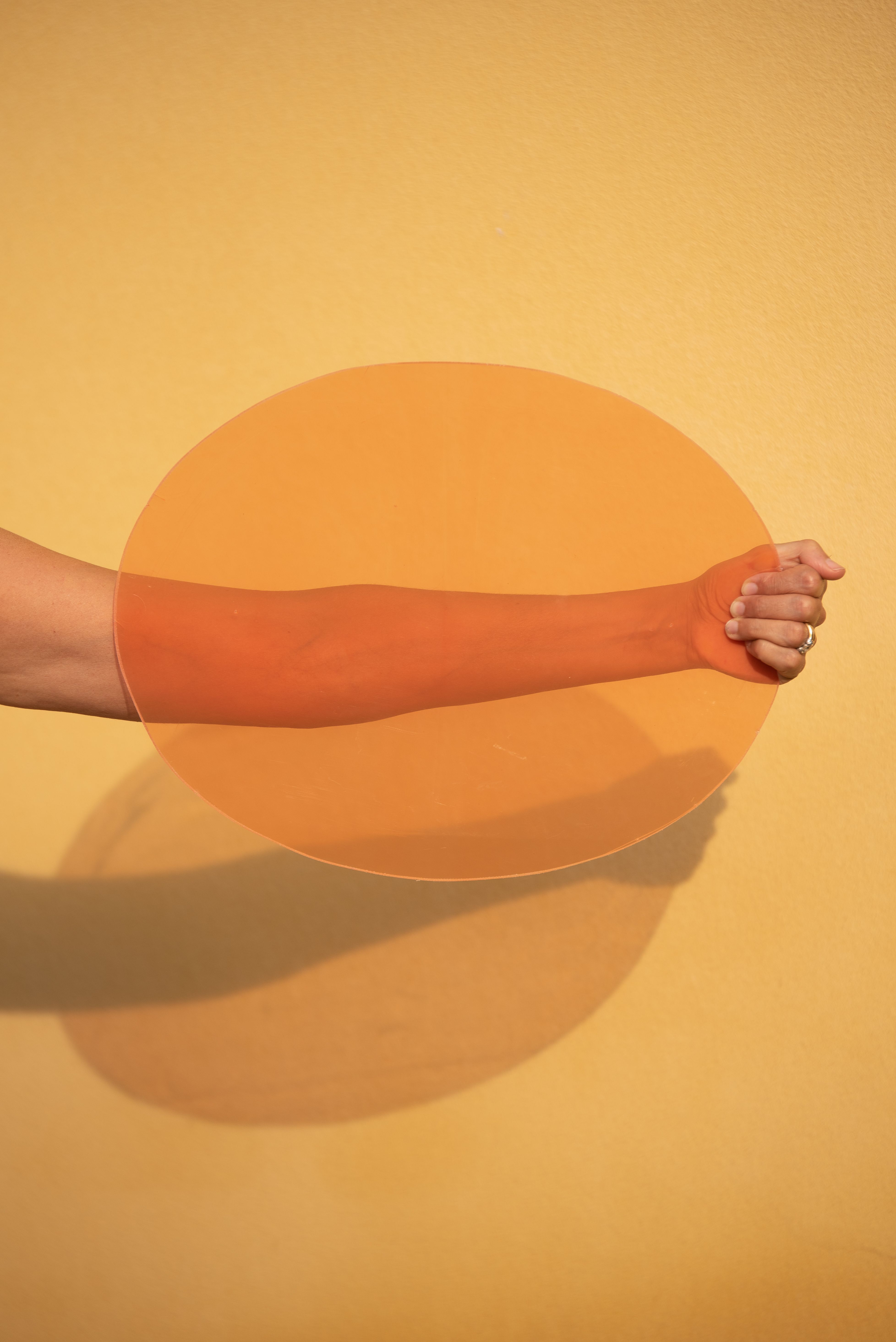 An arm extends through an orange circle against a bright yellow wall, casting a shadow.