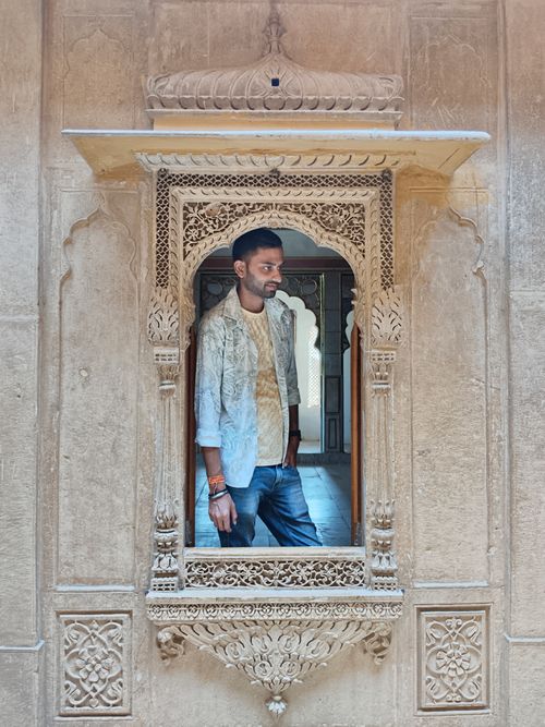 Free Young man stands in an intricately carved stone window, embracing heritage. Stock Photo