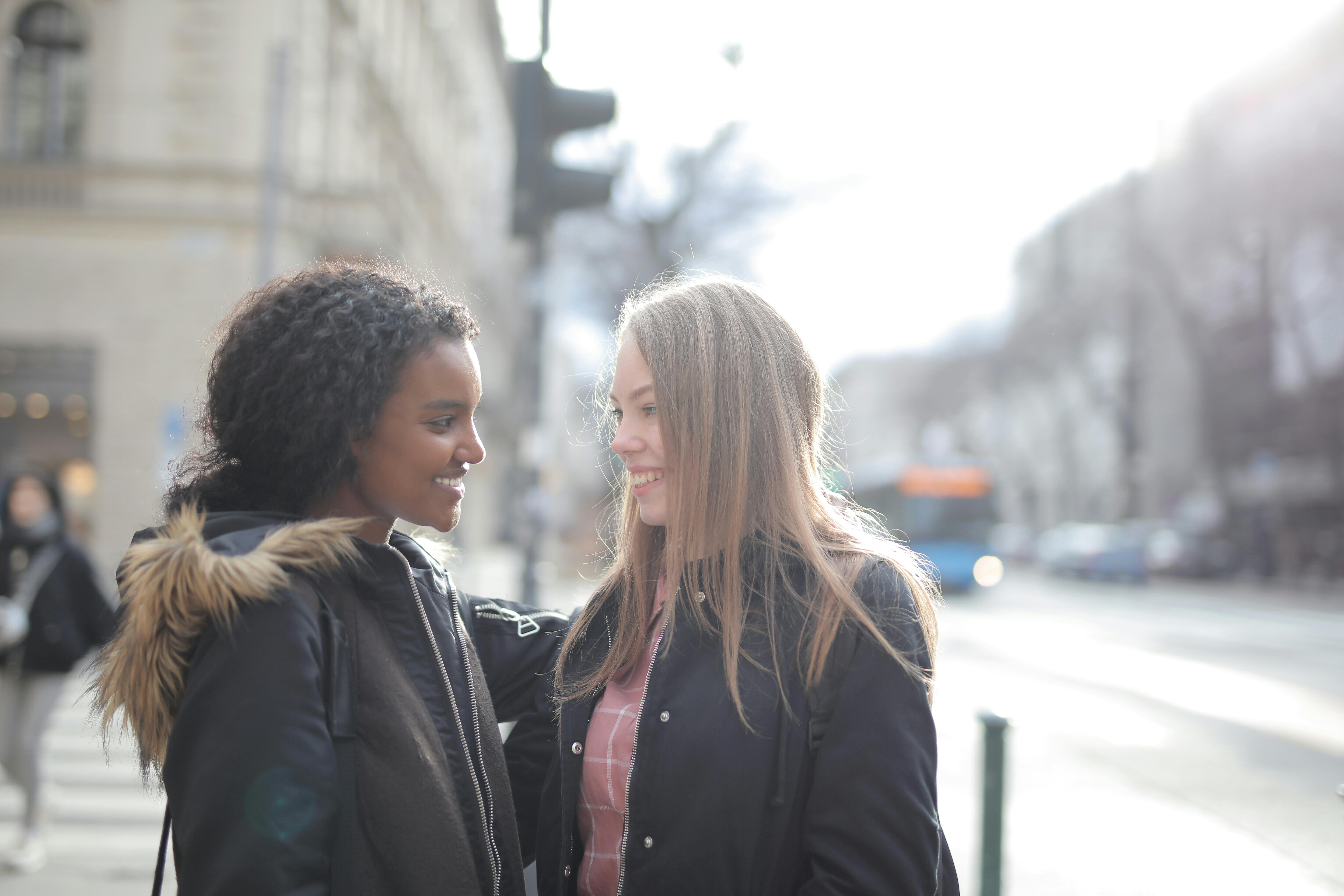 positive multiracial girlfriends standing on sidewalk on street in city