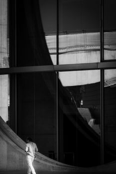 Black and white artistic shot of modern architecture featuring reflections and a solitary person.