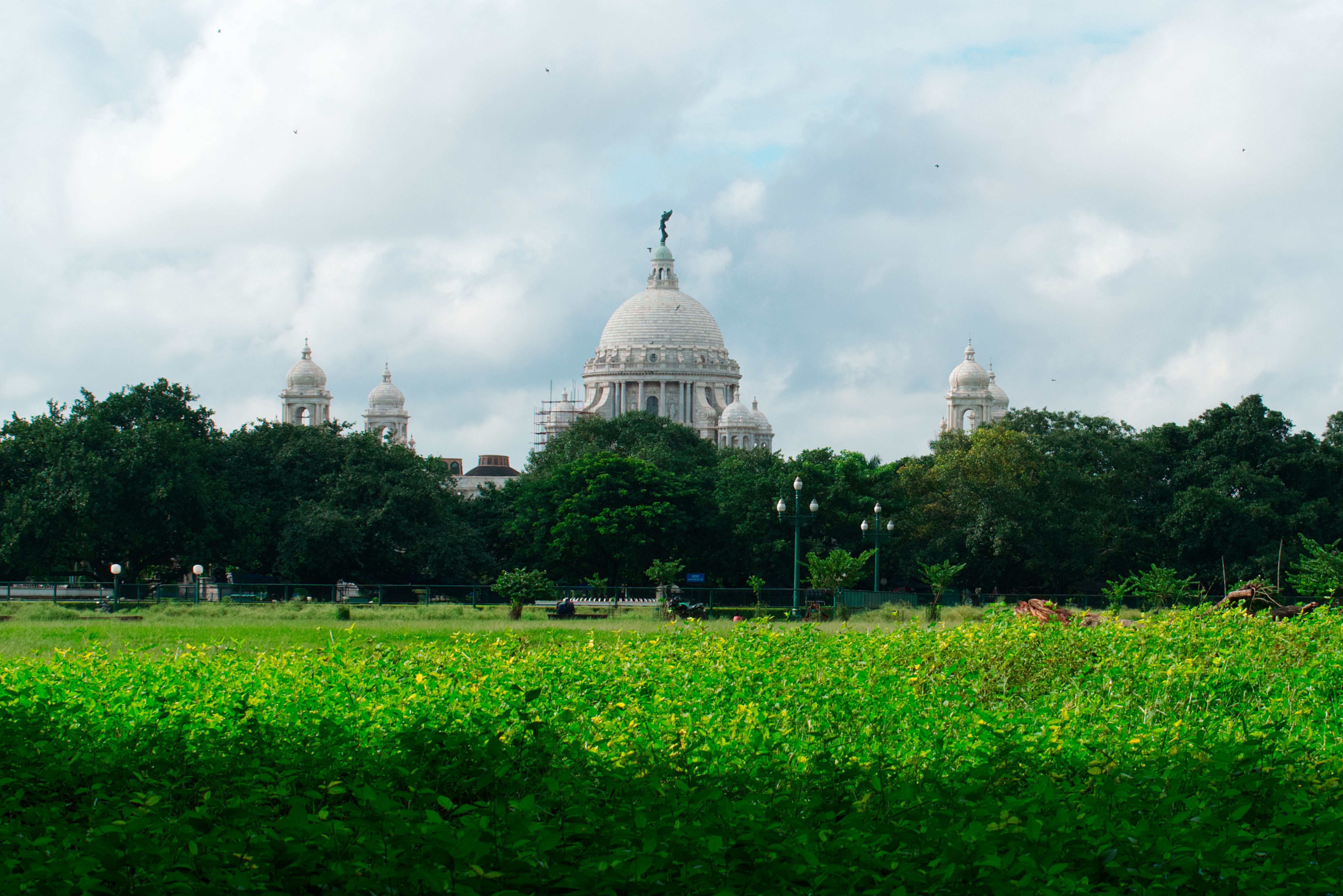 Wide shot of Victoria Memorial in Kolkata, India, with vibrant greenery under a cloudy sky.