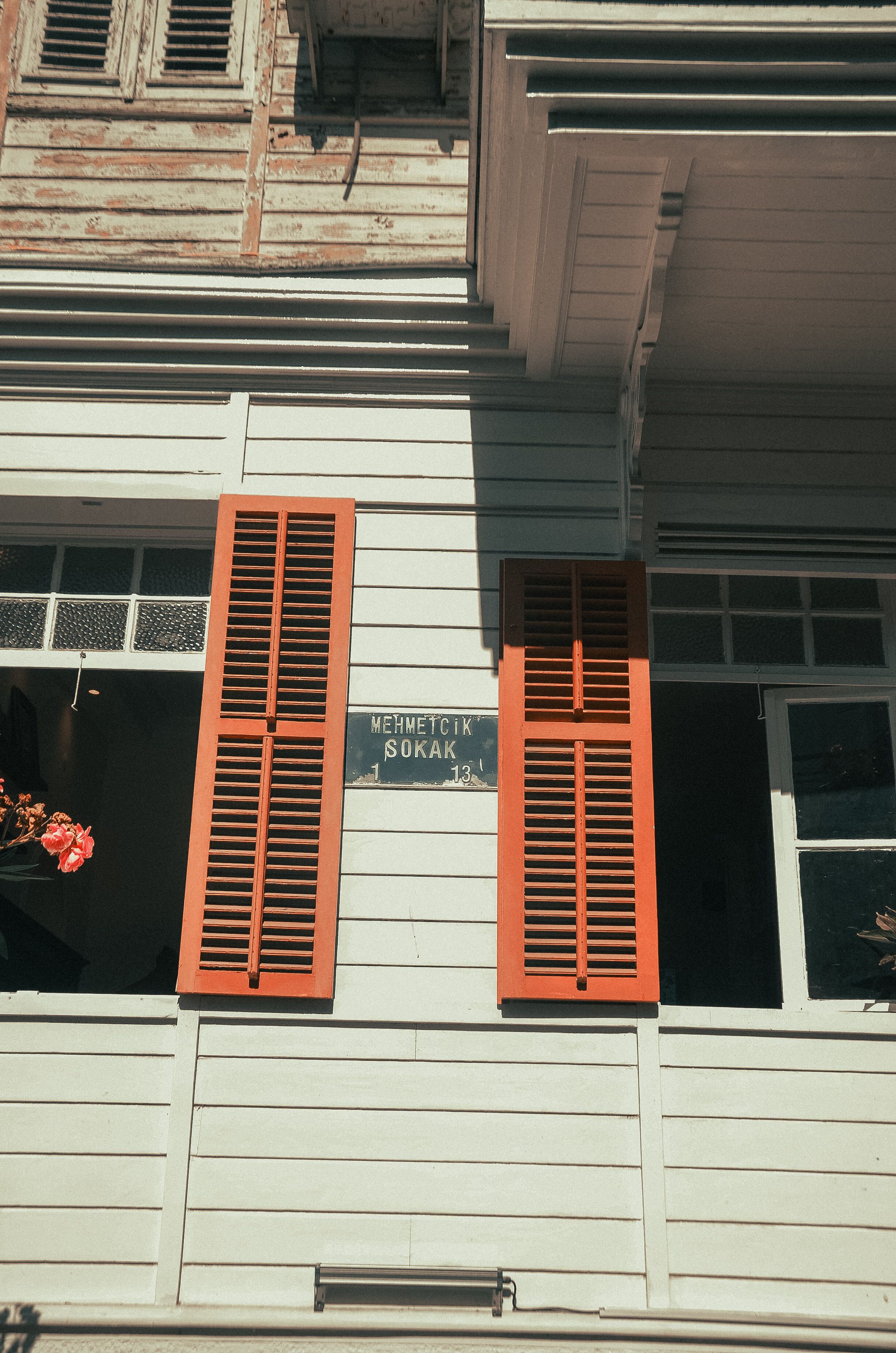 Close-up of a historic wooden house facade featuring bright red shutters and a street sign.
