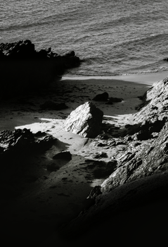 Black and white photo of rugged rocks by the seaside, with dramatic shadows.