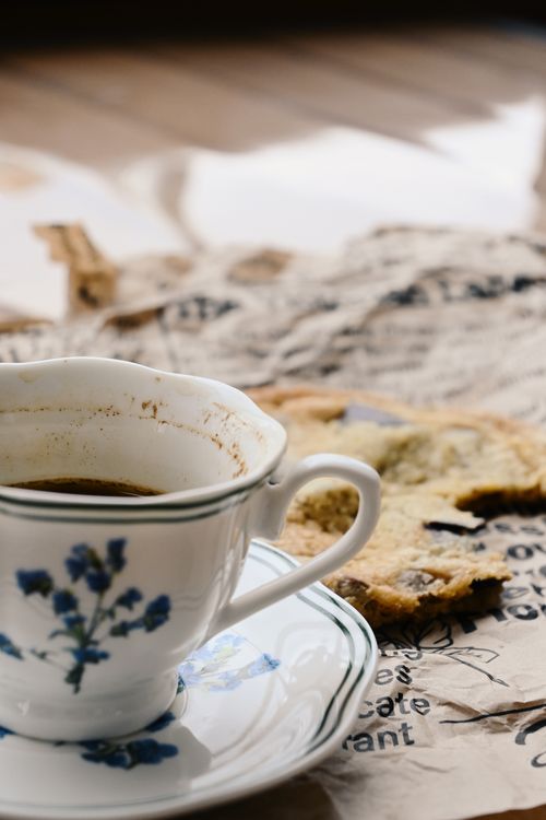 Free Close-up of a floral coffee cup with a biscuit on newspaper, perfect for cozy morning vibes. Stock Photo