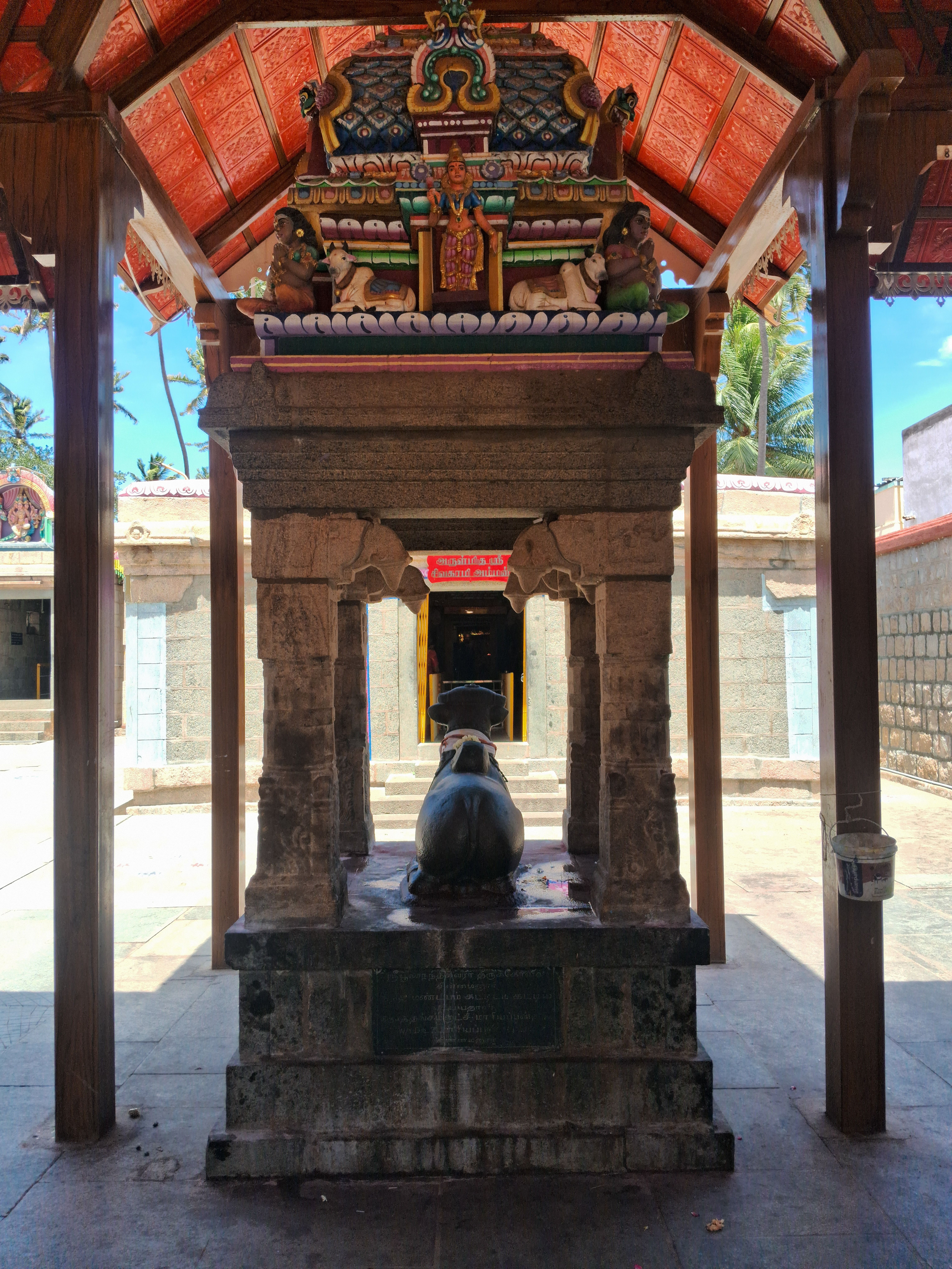 Intricate stone shrine with Nandi statue under a colorful temple roof, reflecting traditional Hindu architecture.