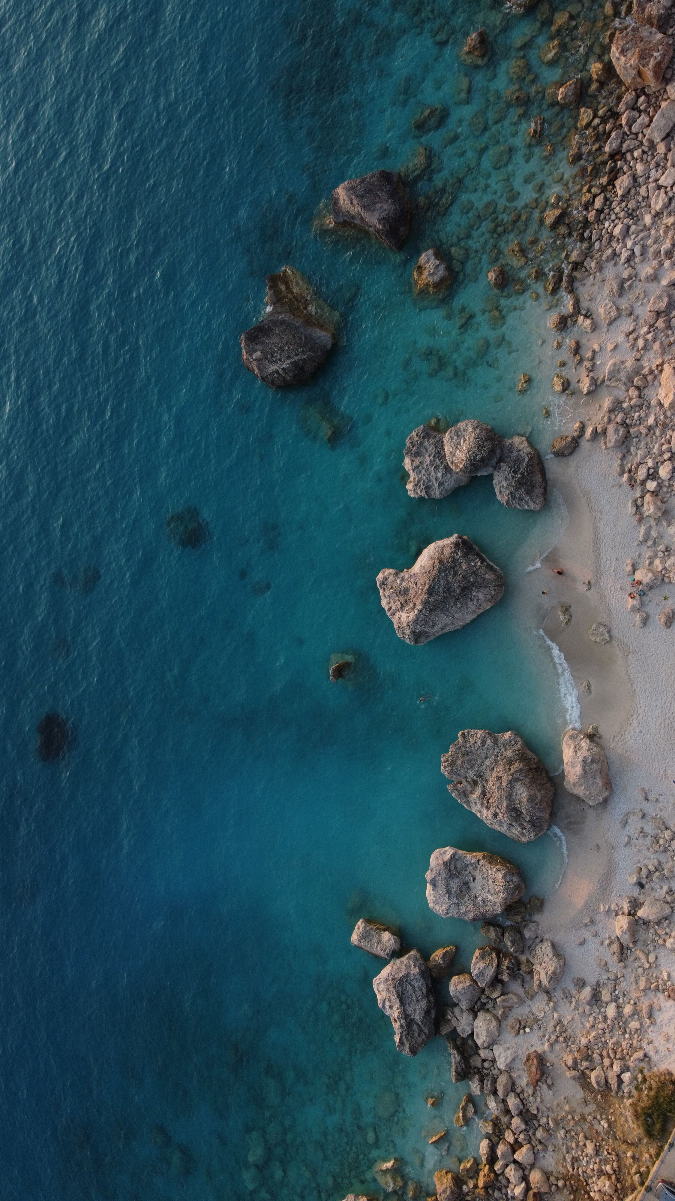 Stunning aerial shot of a rocky coastline with clear blue water and sandy beach.
