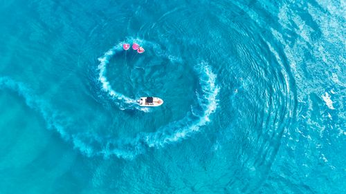 Free Aerial shot of a boat towing tubes creating a circle pattern in the vibrant blue waters of Greece. Stock Photo