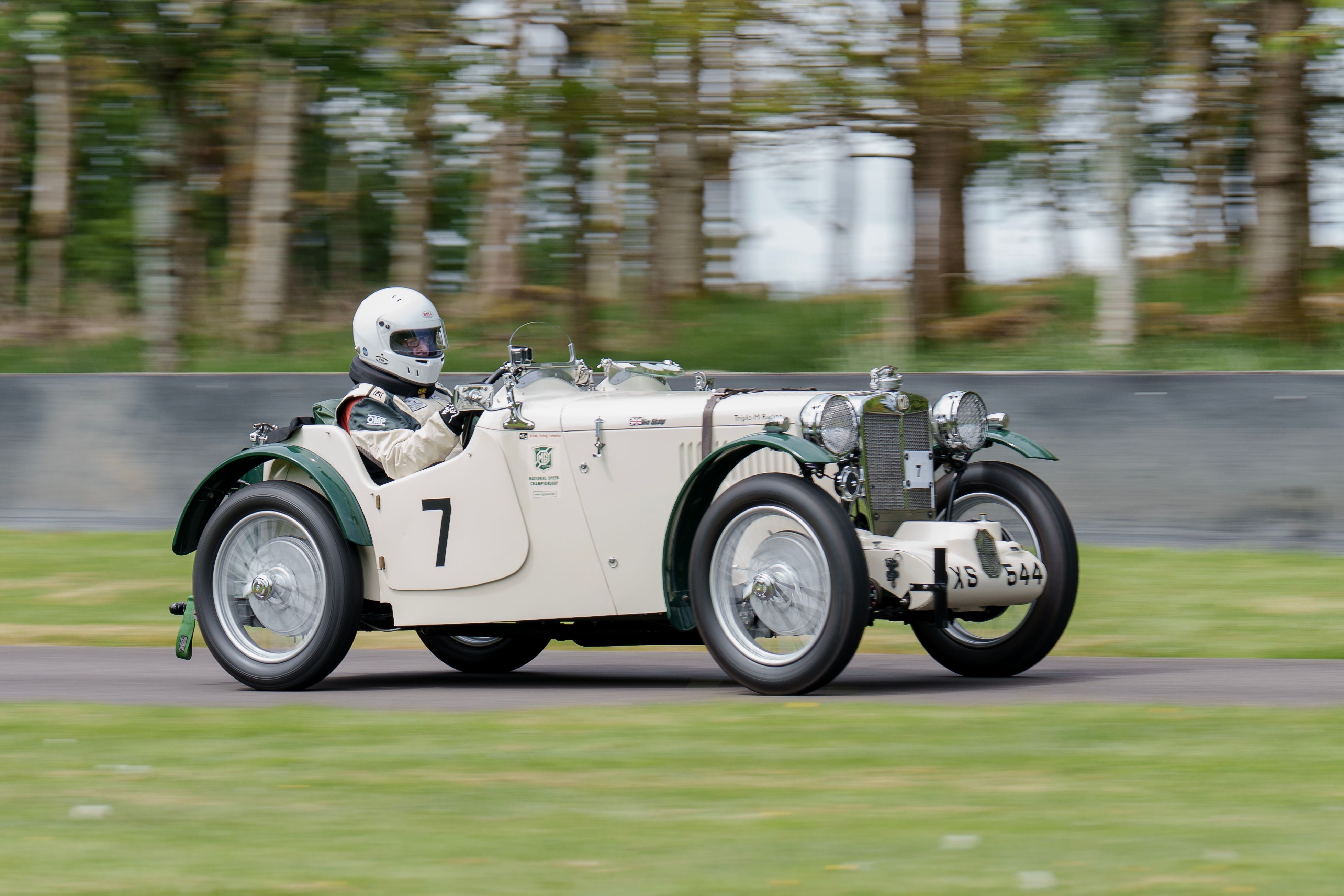 Classic vintage race car speeds on outdoor track during event.