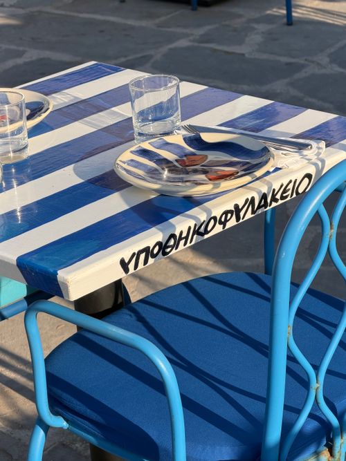 Free Blue and white outdoor café table with Greek writing, evoking sunny Mediterranean vibes. Stock Photo