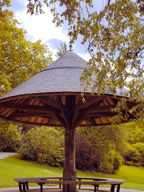 Free A picturesque wooden gazebo surrounded by lush greenery in a sunny park. Stock Photo