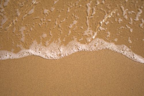 Free Serene image of a gentle ocean wave lapping a sandy beach, embodying relaxation. Stock Photo