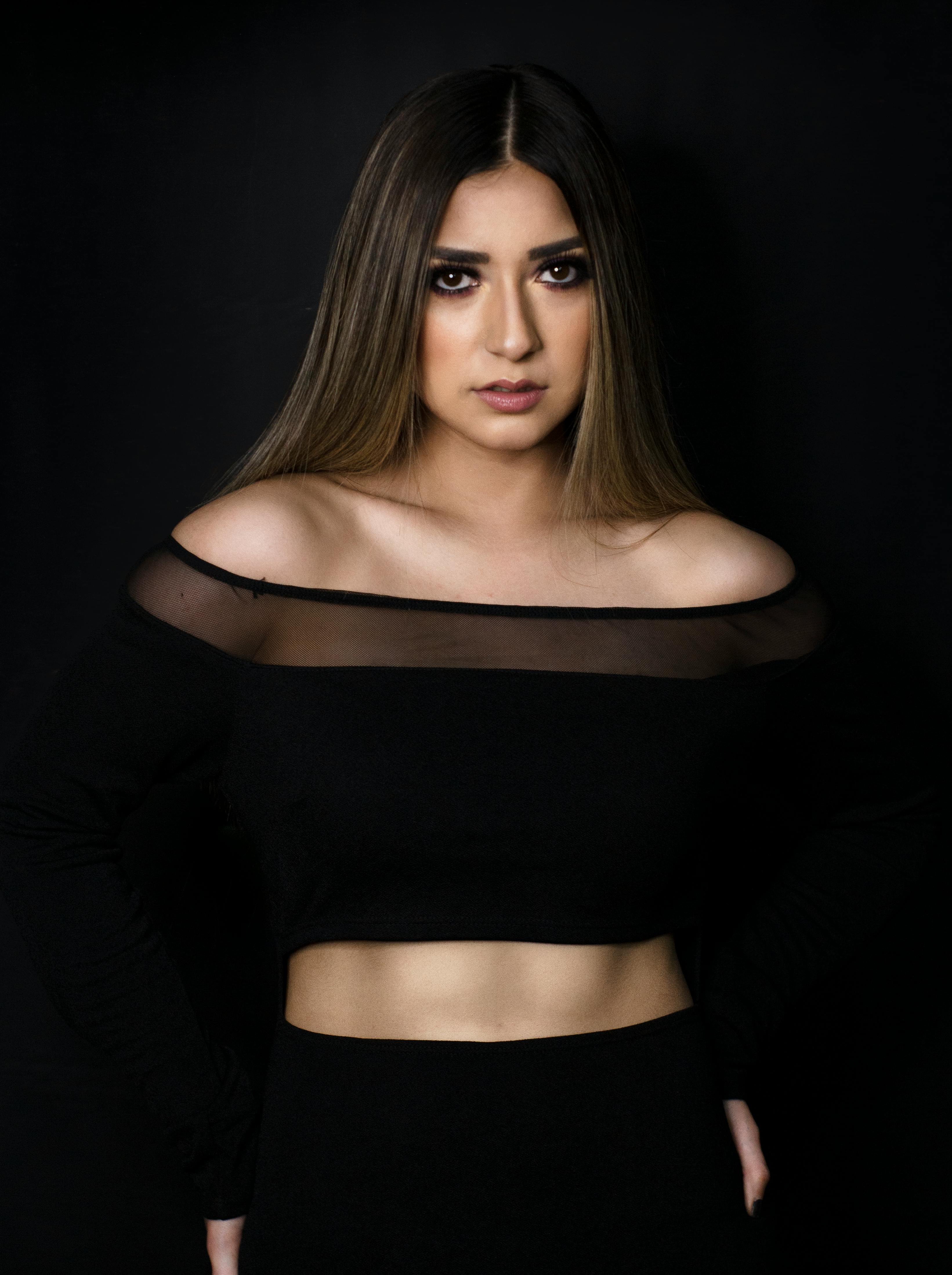 这幅肖像令人惊叹，描绘了一位身着黑色露肩上衣的优雅女性，背景是暗色调