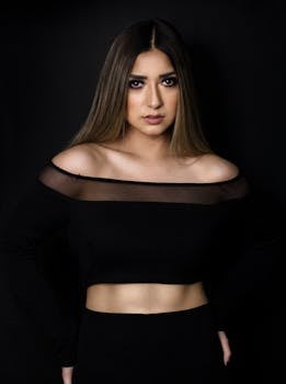 这幅肖像令人惊叹，描绘了一位身着黑色露肩上衣的优雅女性，背景是暗色调