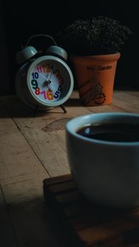 A serene arrangement of coffee, a vintage alarm clock, and a potted plant on a wooden table.