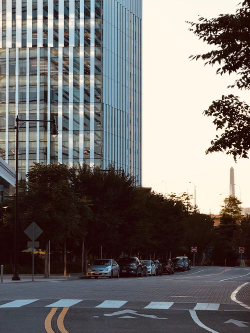 Free City street scene with skyscraper and parked cars at dusk, showcasing urban architecture. Stock Photo