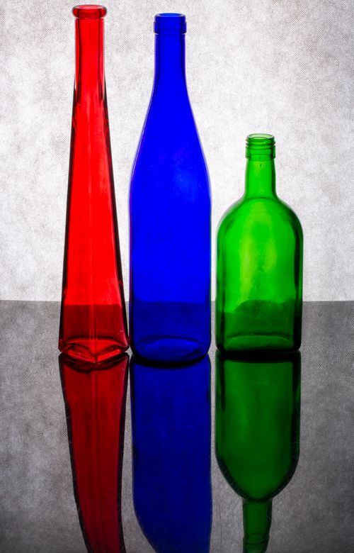 Free Three colorful glass bottles with reflections on a glossy surface against a neutral background. Stock Photo