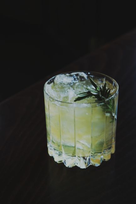 Elegant cocktail with ice cubes and herb garnish on dark background.