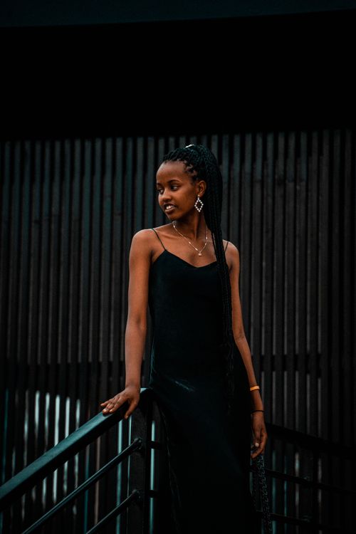Free Stylish Rwandan woman in a black dress poses gracefully with modern architecture backdrop. Stock Photo